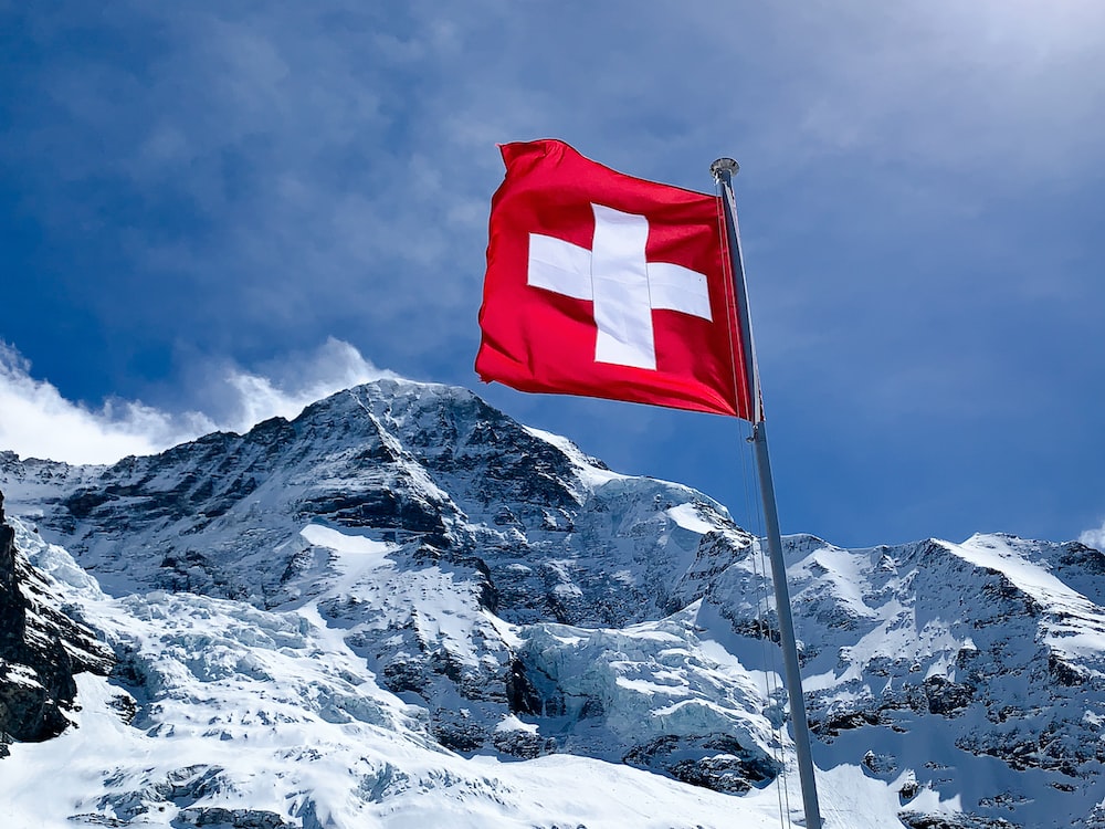 the flag of switzerland, flying in front of a mountain